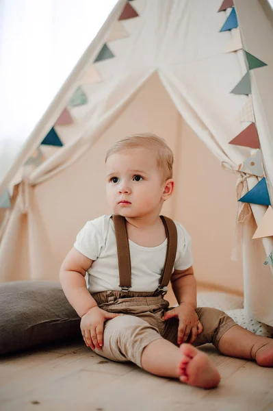 Retrato de adorável menino pequeno feliz sorrindo celebrando 1 ano de aniversário. Um ano de idade europeu pequeno cavalheiro sentado em uma tenda de bebê wigwam — Fotografia de Stock