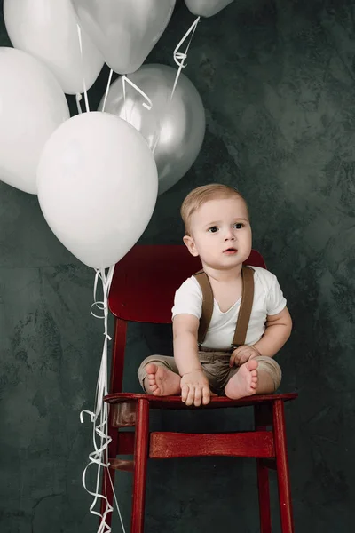 Porträtt av vackra lilla pojke leende firar 1 år Grattis. Ett år gamla europeiska little gentleman sitter i en stol och leker med baloons — Stockfoto