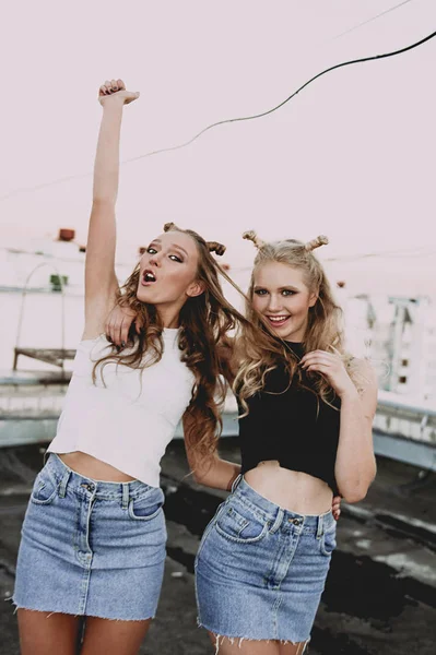 Lifestyle- und People-Konzept: Modeporträt zweier stilvoller Freundinnen in Jeansröcken, draußen auf dem Dach. fröhliche Sommerzeit zum Spaß. Konzept der 90er Jahre. retuschiertes Foto — Stockfoto