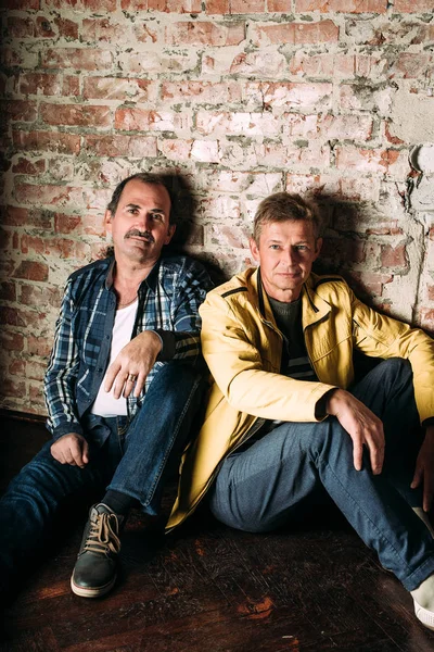 Dos hombres guapos de mediana edad, vestidos con ropa casual, viejos amigos. Fondo de pared de ladrillo rojo . — Foto de Stock