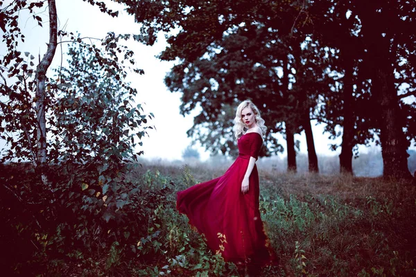 时尚华丽年轻的金发女郎在漂亮的红色裙子，在一个童话般的森林。魔幻的气氛。被修饰调色射击 — 图库照片