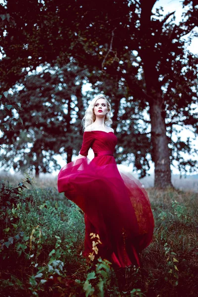 Moda linda jovem loira em belo vestido vermelho em uma floresta de conto de fadas. atmosfera mágica. Tonificação retocada tiro — Fotografia de Stock