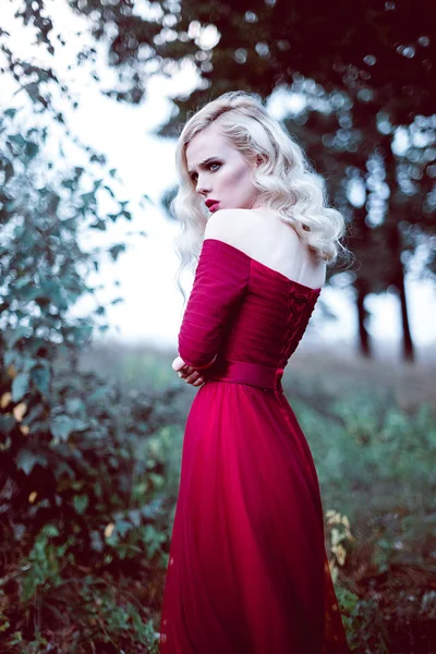 Moda hermosa mujer rubia joven en hermoso vestido rojo en un bosque de cuento de hadas. atmósfera mágica. Disparo de tonificación retocado — Foto de Stock