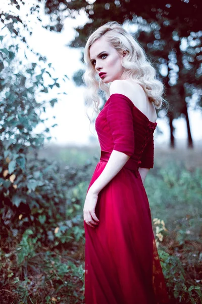 Moda hermosa mujer rubia joven en hermoso vestido rojo en un bosque de cuento de hadas. atmósfera mágica. Disparo de tonificación retocado — Foto de Stock