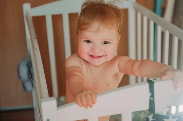 Feliz lindo bebé sonriendo con los dientes y sentado en la cuna, acaba de despertar —  Fotos de Stock