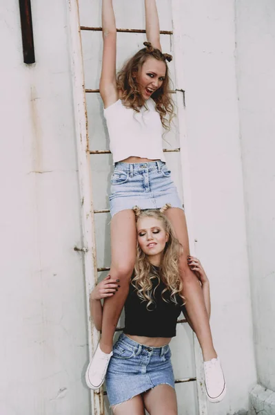 Lifestyle and people concept: Fashion portrait of two stylish girls best friends wearing jeans skirts, outdoors on the roof. Happy summer time for fun. — Stock Photo, Image