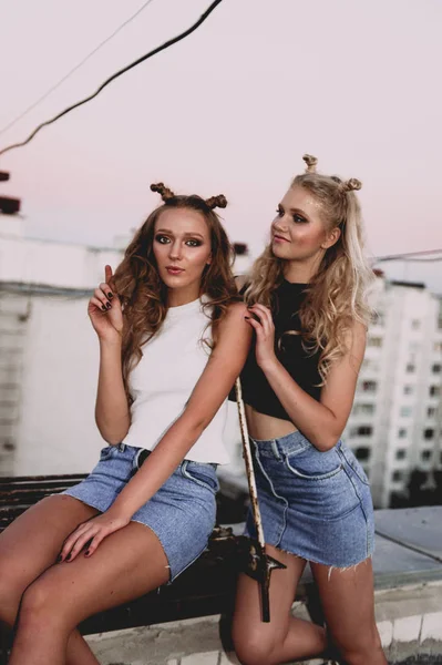 Lifestyle and people concept: Fashion portrait of two stylish girls best friends wearing jeans skirts, outdoors on the roof. Happy summer time for fun. — Stock Photo, Image