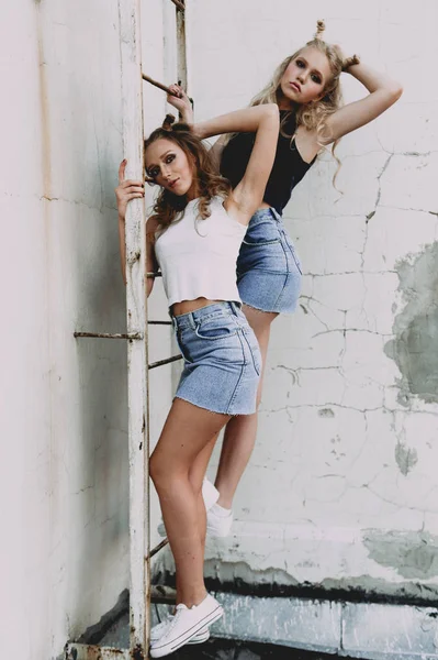 Lifestyle- und People-Konzept: Modeporträt zweier stilvoller Freundinnen in Jeansröcken, draußen auf dem Dach. fröhliche Sommerzeit zum Spaß. — Stockfoto