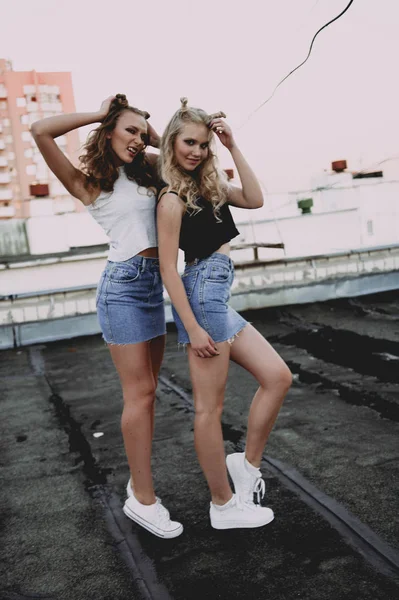 Lifestyle and people concept: Fashion portrait of two stylish girls best friends wearing jeans skirts, outdoors on the roof. Happy summer time for fun. — Stock Photo, Image