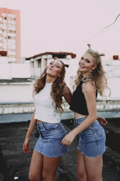 Lifestyle and people concept: Fashion portrait of two stylish girls best friends wearing jeans skirts, outdoors on the roof. Happy summer time for fun. — Stock Photo, Image