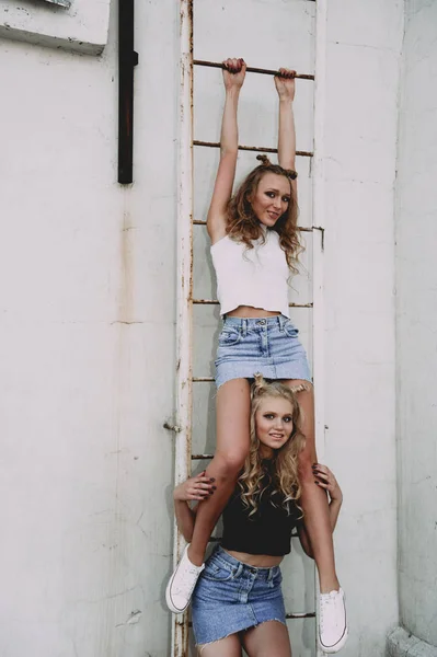 Lifestyle and people concept: Fashion portrait of two stylish girls best friends wearing jeans skirts, outdoors on the roof. Happy summer time for fun. — Stock Photo, Image