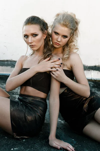 Glamour make-up twee vrouwen met lange haren stijl zittend op straat muur achtergrond in donker. Fashion kleur portret — Stockfoto