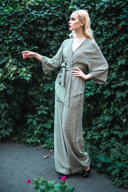 Kırmızı ruj büyük parlak gözleri olan, genç güzel sarışın kız ve ayar güneş trendy kıyafetler, yeşil arka plan poz kostüm yapmak