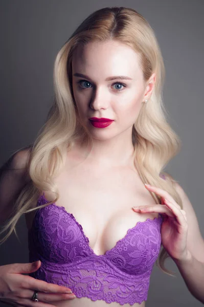 Fille modèle de beauté avec des lèvres rouges maquillage parfait et les yeux bleus regardant la caméra, portant un soutien-gorge magenta. Portrait de jolie jeune femme sexy aux cheveux blonds. Belle visage féminin avec sk frais clair — Photo