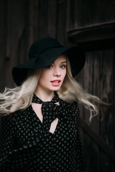 Krásná atraktivní a elegantní dívka, která nosí černý klobouk postavení pózuje v městě. Nahé líčení, denní účes a styl země velké módní glamour. — Stock fotografie