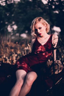 Kırmızı dudaklar ve saç ile güzel ve zarif sarışın kadın giyiyor şarap kırmızı gece sonbahar, retro vintage tarzı ve moda yatakta açık havada poz dalgalar.