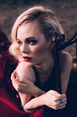 Kırmızı dudaklar ve saç ile güzel ve zarif sarışın kadın giyiyor şarap kırmızı gece sonbahar, retro vintage tarzı ve moda yatakta açık havada poz dalgalar.