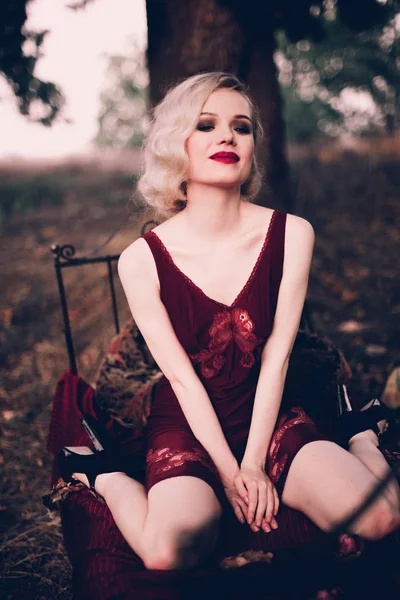 美しく、エレガントな赤い唇と髪とブロンドの女性波秋、レトロなビンテージ スタイルとファッション屋外ベッドでポーズ着てワイン赤いネグリジェ. — ストック写真