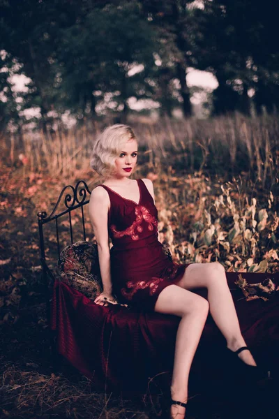 Mujer rubia hermosa y elegante con labios rojos y olas de pelo usando camisón rojo vino posando en la cama al aire libre otoño, estilo vintage retro y moda . — Foto de Stock