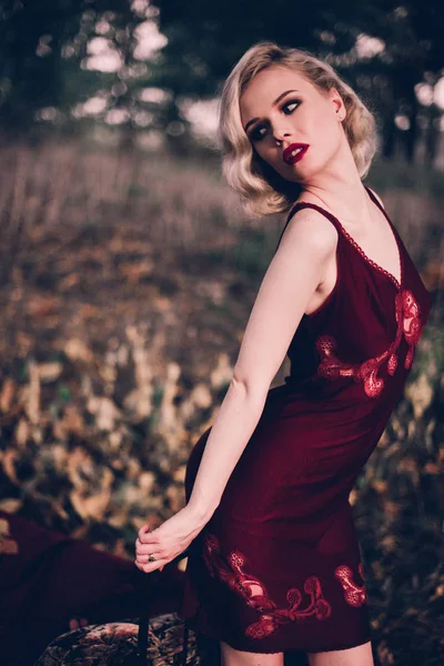 美しく、エレガントな赤い唇と髪とブロンドの女性波秋、レトロなビンテージ スタイルとファッション屋外ベッドでポーズ着てワイン赤いネグリジェ. — ストック写真
