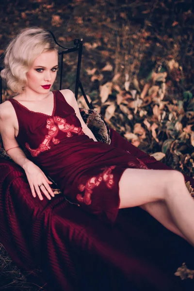 Mujer rubia hermosa y elegante con labios rojos y olas de pelo usando camisón rojo vino posando en la cama al aire libre otoño, estilo vintage retro y moda . —  Fotos de Stock