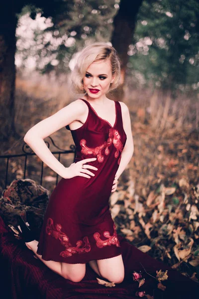 Mujer rubia hermosa y elegante con labios rojos y olas de pelo usando camisón rojo vino posando en la cama al aire libre otoño, estilo vintage retro y moda . — Foto de Stock