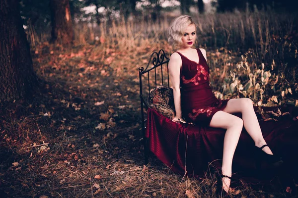 Mooi en elegant blonde vrouw met rode lippen en haren golven dragen wijn rode nachtjapon poseren op het bed buitenshuis herfst, retro vintage stijl en mode. — Stockfoto