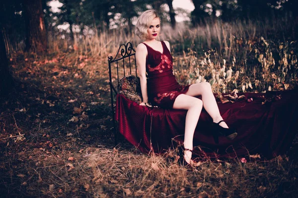 Mujer rubia hermosa y elegante con labios rojos y olas de pelo usando camisón rojo vino posando en la cama al aire libre otoño, estilo vintage retro y moda . —  Fotos de Stock