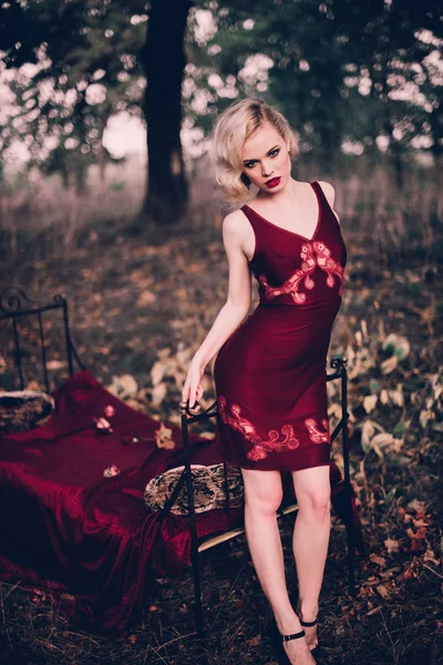 Mujer rubia hermosa y elegante con labios rojos y olas de pelo usando camisón rojo vino posando en la cama al aire libre otoño, estilo vintage retro y moda . — Foto de Stock