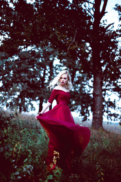 Модная красивая молодая блондинка в красивом красном платье в сказочном лесу. волшебная атмосфера. тонизирующий выстрел
