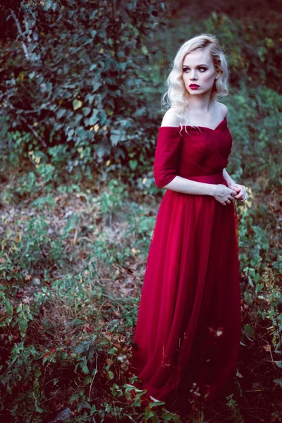 Moda splendida giovane donna bionda in bellissimo vestito rosso in una foresta da favola. atmosfera magica. colpo tonificante — Foto Stock