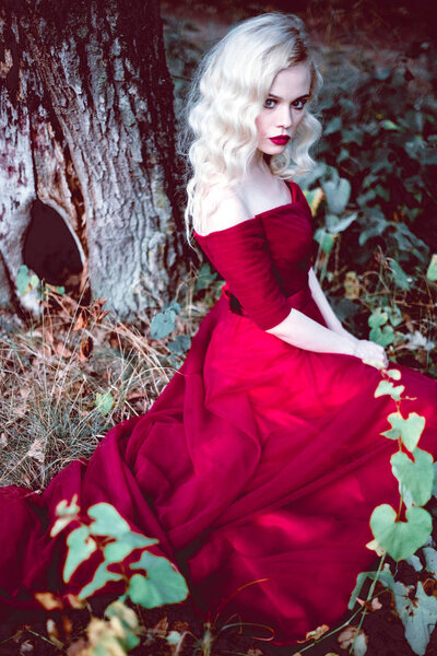 Fashion gorgeous young blonde woman in beautiful red dress in a fairy-tale forest. magic atmosphere