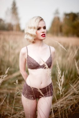 Güzel ve zarif gülümseyen seksi sarışın kadın kırmızı dudaklar ve saç giyen bej liingerie yaz, retro vintage tarzı ve moda alanında açık havada poz dalgalar. Sho tonlama düzeltisiz Güzel Sanatlar