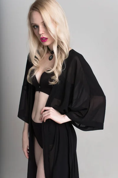 Jeune femme blonde souriante sexy en lingerie noire posant sur fond blanc . — Photo
