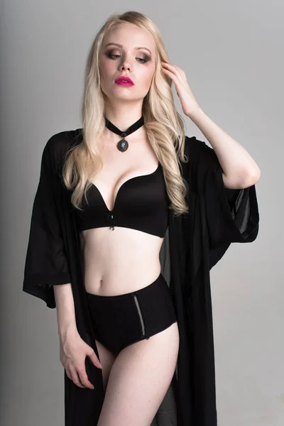 Jonge sexy lachende blonde vrouw in zwarte lingerie die zich voordeed op witte achtergrond. — Stockfoto