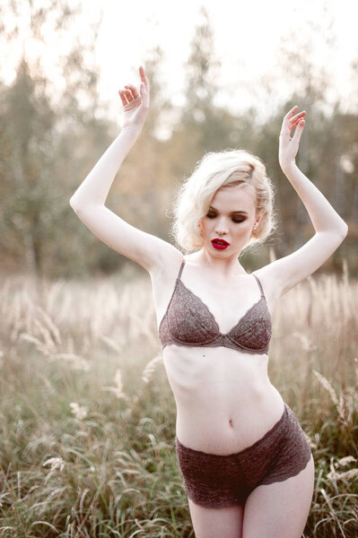 Beautiful and elegant smiling sexy blonde woman with red lips and hair waves wearing beige liingerie posing on the field outdoors summer, retro vintage style and fashion. Retouched fine art toning sho