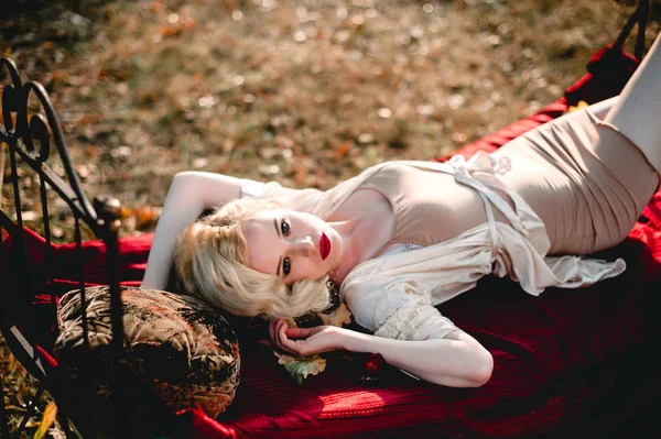 Mujer rubia hermosa y elegante con labios rojos y ondas de pelo usando camisón beige posando en la cama al aire libre otoño, estilo vintage retro y moda. arte fino tonificación tiro — Foto de Stock