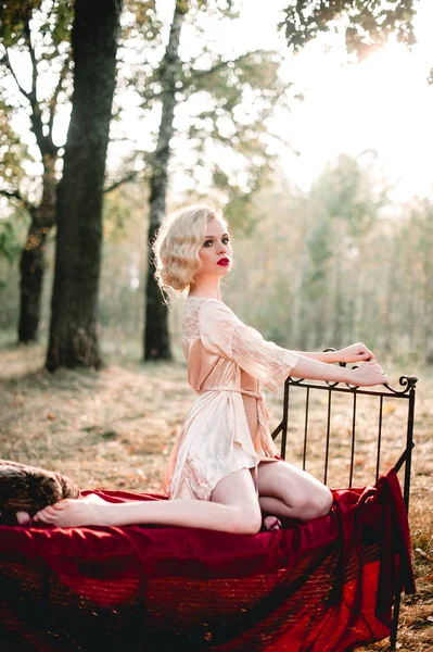 Mujer rubia hermosa y elegante con labios rojos y ondas de pelo usando camisón beige posando en la cama al aire libre otoño, estilo vintage retro y moda. arte fino tonificación tiro — Foto de Stock