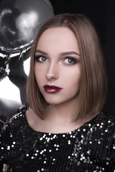 Close up retrato de moda de uma jovem linda menina elegante com festa brilhante compõem em cima de lantejoulas pretas à noite. Ela está mantendo estrelas de prata balões em sua mão. Uma rapariga na festa. Tiro retocado — Fotografia de Stock