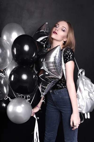 Close up fashion portrait of a young beautiful elegant girl with bright party make up in evening black sequin top. She is keeping silver stars balloons in her hand. Girl at the party. Retouched shot
