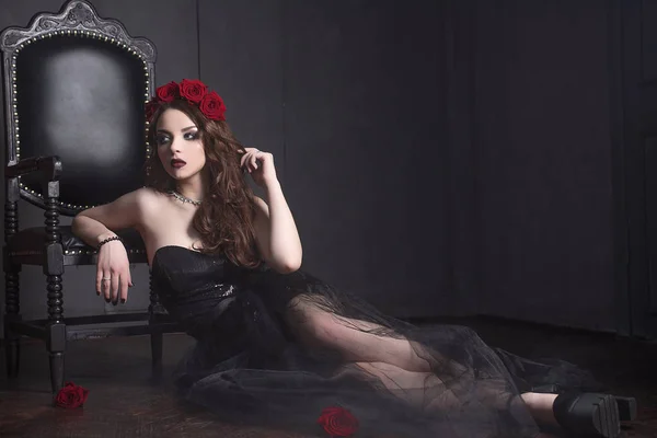 Mooie jonge vrouw met rozen bloem in de haren, zwarte jurk met make-up dragen over donkere achtergrond, gotische sfeer. donker rood lips.close-up mode geretoucheerd portret — Stockfoto