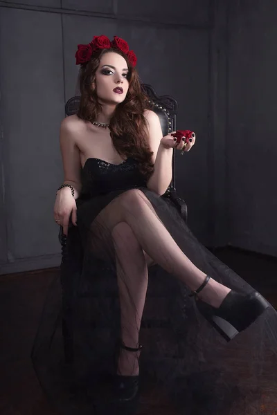 Bela jovem com flores de rosas no cabelo, vestindo vestido preto com maquiagem sobre fundo escuro, atmosfera gótica. lips.close-up vermelho escuro moda retocada retrato — Fotografia de Stock