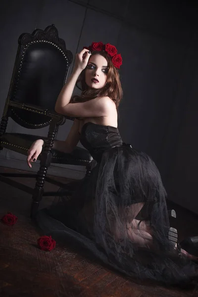 Vacker ung kvinna med rosor blomma i hår, klädd i svart klänning med make-up över mörk bakgrund, gotisk atmosfär. mörk röd lips.close-up mode retuscherade porträtt — Stockfoto