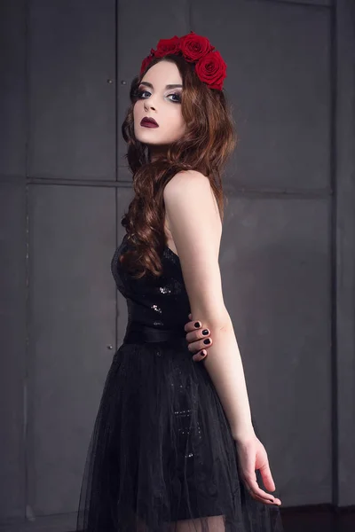 Όμορφη νεαρή γυναίκα με τριαντάφυλλα λουλούδι στα μαλλιά, φορώντας μαύρο φόρεμα με μακιγιάζ σε σκούρο φόντο, gothic ατμόσφαιρα. σκούρο κόκκινο lips.close-up μόδας retouched πορτρέτο — Φωτογραφία Αρχείου