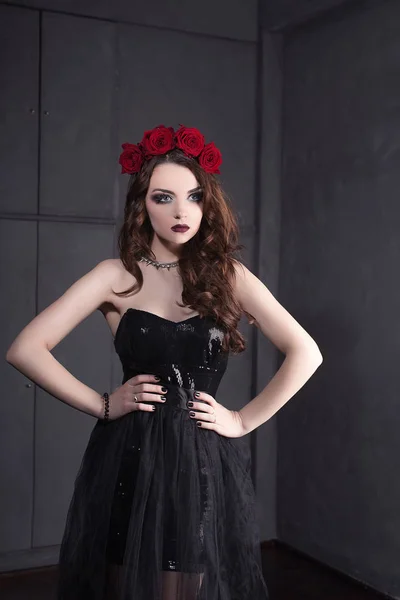 Femeie tânără frumoasă cu flori de trandafiri în păr, purtând rochie neagră cu machiaj pe fundal întunecat, atmosferă gotică. buze roșiate.close-up de moda retușate portret — Fotografie, imagine de stoc