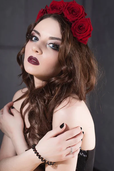 Hermosa joven con flores de rosas en el pelo. chica de belleza con maquillaje sobre fondo oscuro. rojo oscuro lips.close-up retrato retocado de moda — Foto de Stock