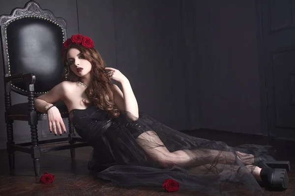Bela jovem com flores de rosas no cabelo, vestindo vestido preto com maquiagem sobre fundo escuro, atmosfera gótica. lips.close-up vermelho escuro moda retocada retrato — Fotografia de Stock