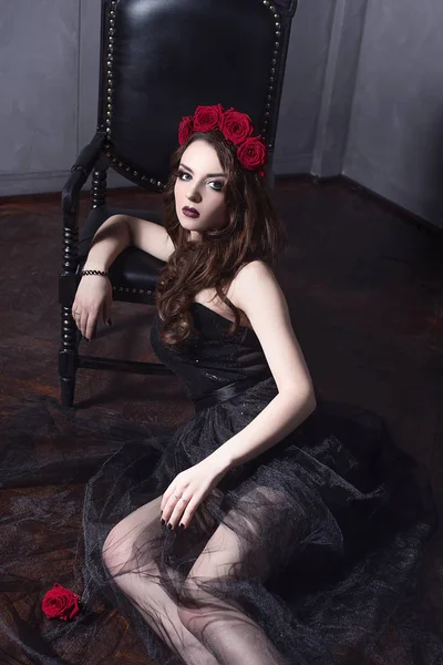 Schöne junge Frau mit Rosen Blume im Haar, trägt schwarzes Kleid mit Make-up vor dunklem Hintergrund, gotische Atmosphäre. dunkelrote Lippen.Nahaufnahme Mode retuschiert Porträt — Stockfoto