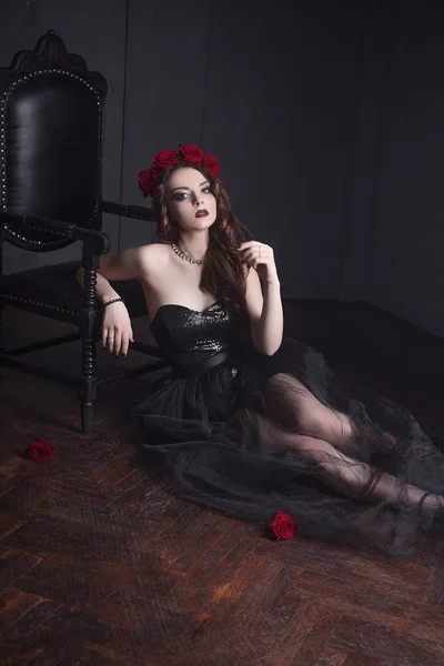 Όμορφη νεαρή γυναίκα με τριαντάφυλλα λουλούδι στα μαλλιά, φορώντας μαύρο φόρεμα με μακιγιάζ σε σκούρο φόντο, gothic ατμόσφαιρα. σκούρο κόκκινο lips.close-up μόδας retouched πορτρέτο — Φωτογραφία Αρχείου