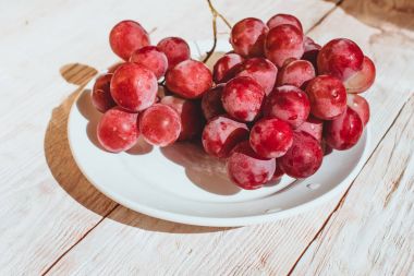 Ahşap masa, flatlay bir tabak taze kırmızı üzüm